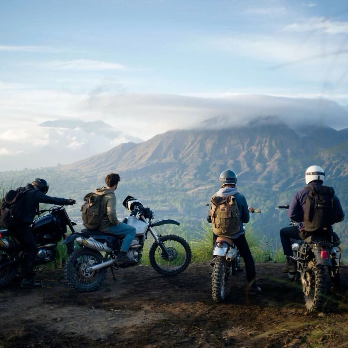 Riders on dirt bikes looking out at a volcano at sunrise